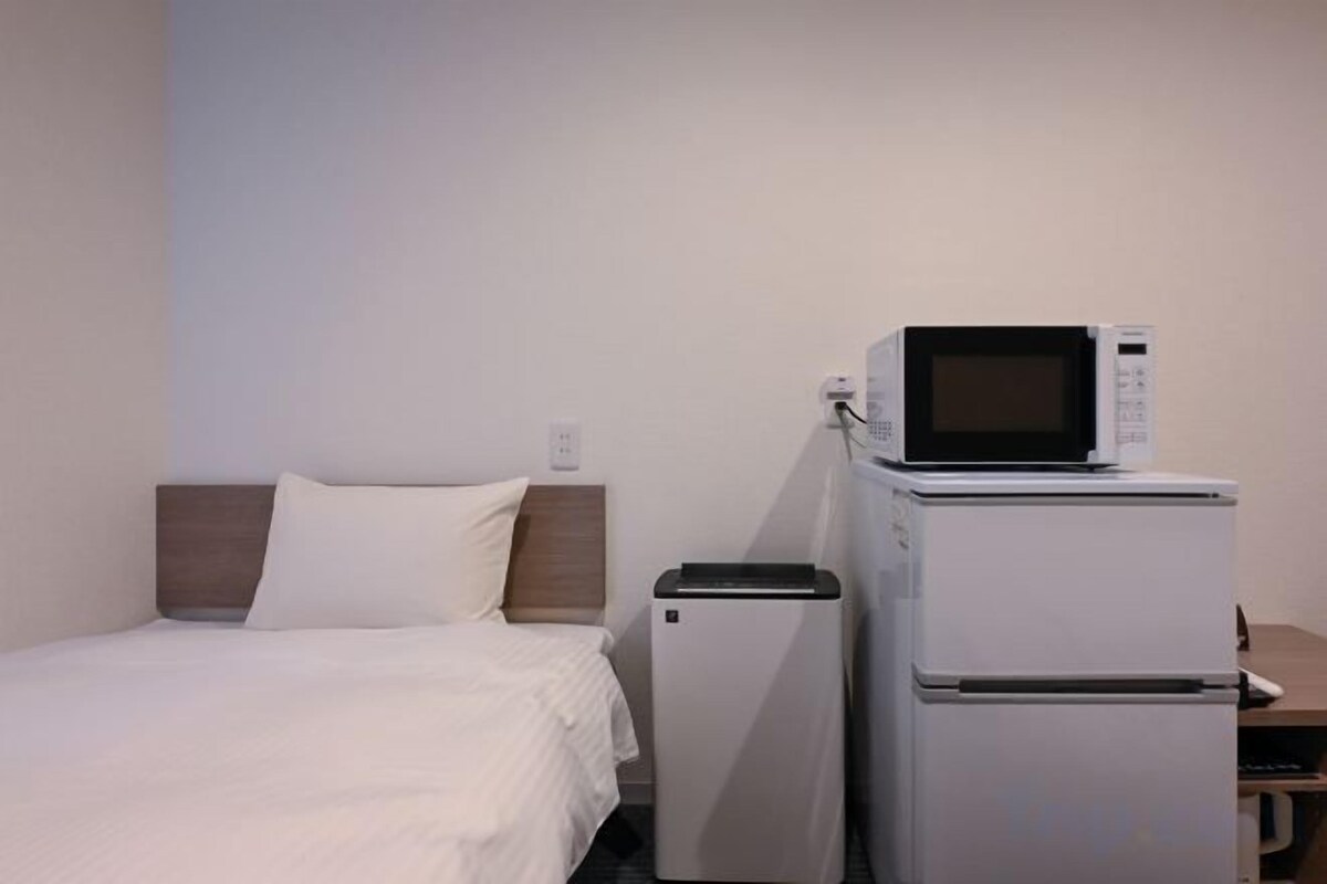 A hotel room with a bed, a microwave, and a refrigerator.