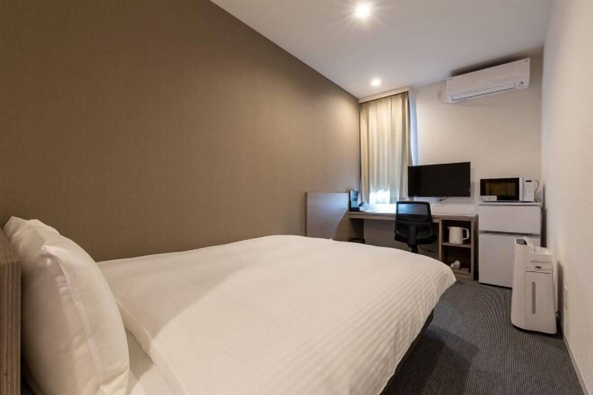 A hotel room with a large bed, a desk with a computer, a television, and a microwave.