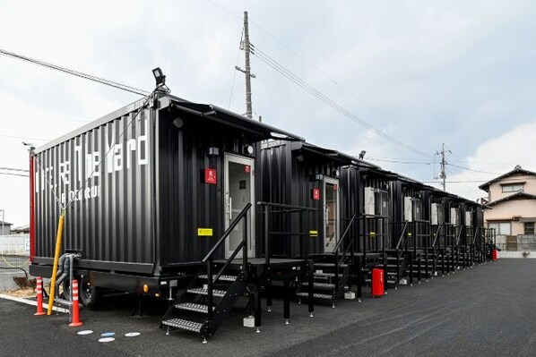 Eine Reihe schwarzer Zugwagons mit Außentreppen und einer kleinen Tür, geparkt auf einer befestigten Fläche, mit einem Gebäude im Hintergrund.