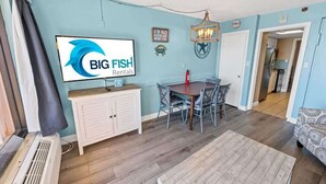 En stue med spiseplads, et fjernsyn monteret på væggen, en lysekrone og et skilt for Big Fish Rentals.