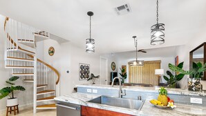 A kitchen with a marble countertop, stainless steel sink, wooden cabinets, and a spiral staircase. - Renovated Penthouse Lake & Golf Course Views AC Near Bay - Vrkcv (Waikoloa)