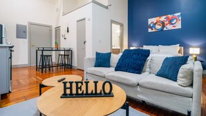 A modern living room with a sofa, a coffee table, and a 'HELLO' sign. There is a painting on the wall and a lamp on the side table. - Near Hospitals & DT  ~  Vibey+Parking+W/D+Churchill (Louisville)