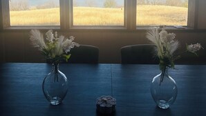 A room with three large windows offering a view of a field and a body of water. There are two vases with flowers on a table. - Private and Unique 14 acre European Lakefront Villa in Texas! (Hubbard)
