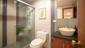 A modern bathroom with a glass-enclosed shower, a toilet, a sink, and a framed plant on the wall. - Gran Esmeralda Space View and Style (Cuenca)
