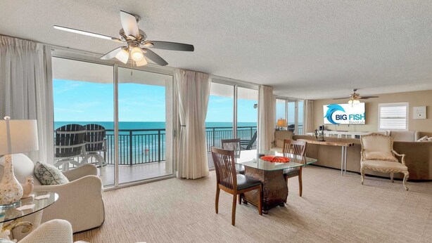Ein Hotelzimmer mit Balkon, Essbereich und einem Fernseher, der 'BIG FISH Rentals' anzeigt.