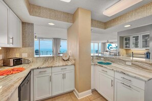 A modern kitchen with white cabinets, a marble countertop, and a view of the ocean.