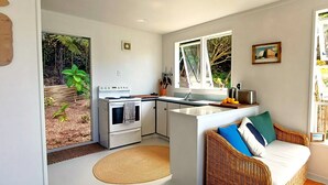 Een compacte keuken met een centraal eiland, een zithoek met een rieten bank en grote ramen met uitzicht op de omgeving.