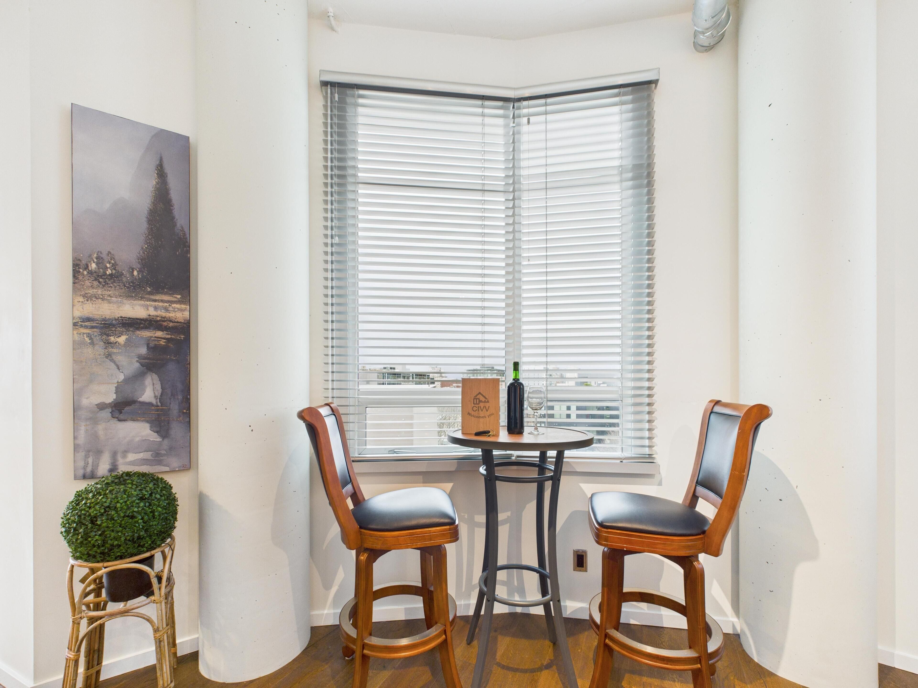 Een hoekkamer met erker, twee houten stoelen, een tafeltje met fles en glas, en een lijst met een afbeelding aan de muur.