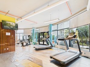 A modern gym with treadmills, stationary bikes, and a large window offering a view of the outdoors. - Your Private Downtown Oasis (Victoria South)