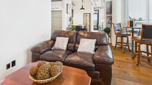 A modern living room with a leather sofa, wooden dining table, and a view of the kitchen and dining area. - Your Private Downtown Oasis (Victoria South)