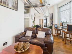 A modern living room with a leather sofa, wooden dining table, and a view of the kitchen and dining area. - Your Private Downtown Oasis (Victoria South)