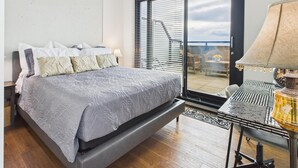 A bedroom with a bed, a desk with a lamp, and a view of the outdoors through a sliding door. - Your Private Downtown Oasis (Victoria South)