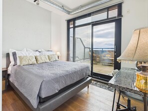 A bedroom with a bed, a desk with a lamp, and a view of the outdoors through a sliding door. - Your Private Downtown Oasis (Victoria South)
