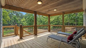 Eine Holzterrasse mit zwei Liegestühlen und einem Geländer, mit Blick auf ein bewaldetes Gebiet.