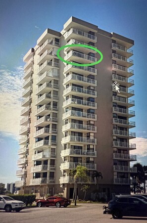 A high-rise building with multiple balconies, a clear sky, and parked cars in the foreground. - Cozy beach condo on desirable Fort Myers Beach - Unit 1107 (Fort Myers Beach)