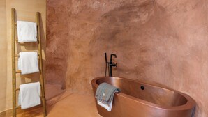 A bathroom with a copper bathtub, a wooden towel rack with three towels, and a textured wall. - Honey Rock Landing (Delta)