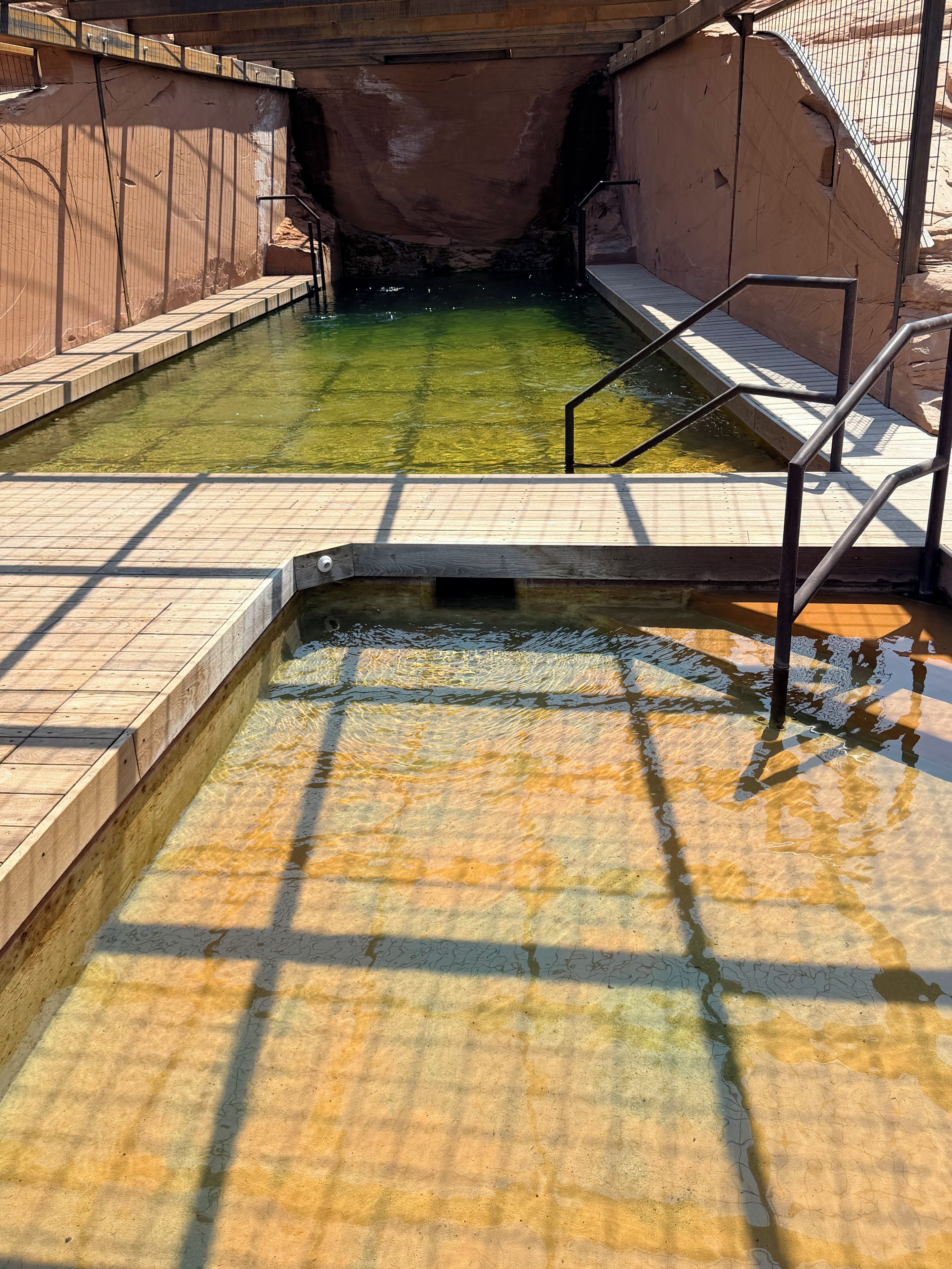 A pool area with clear water, wooden steps, and metal railings.