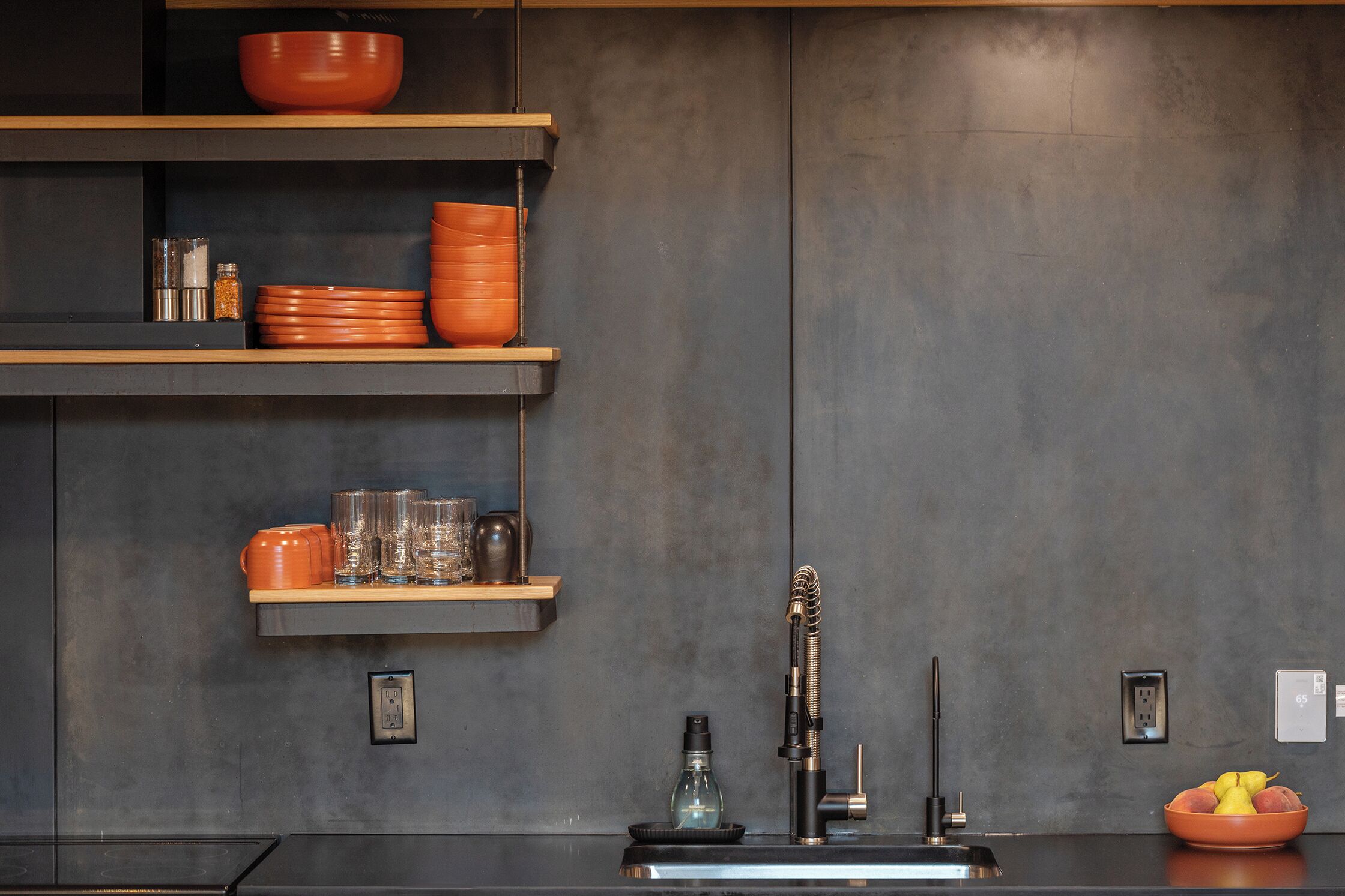 Una cocina con paredes oscuras, estantes de madera y un grifo moderno.