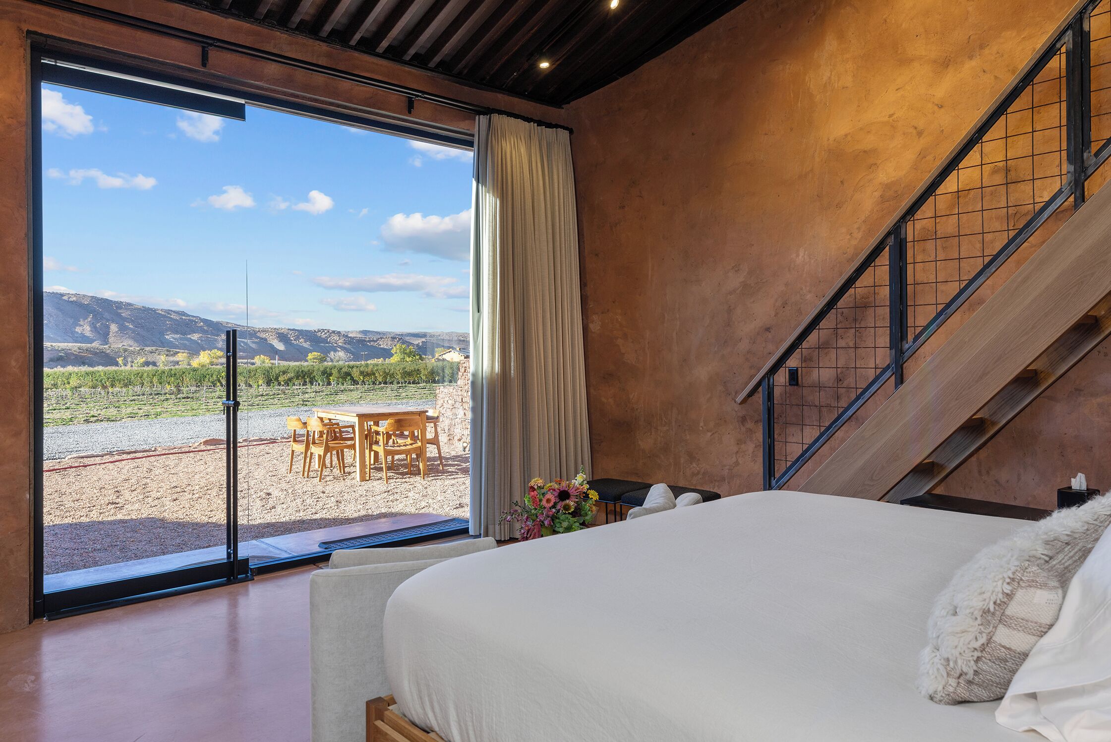 Ein Schlafzimmer mit einem großen Bett, Blick auf einen Weinberg und einer Treppe.