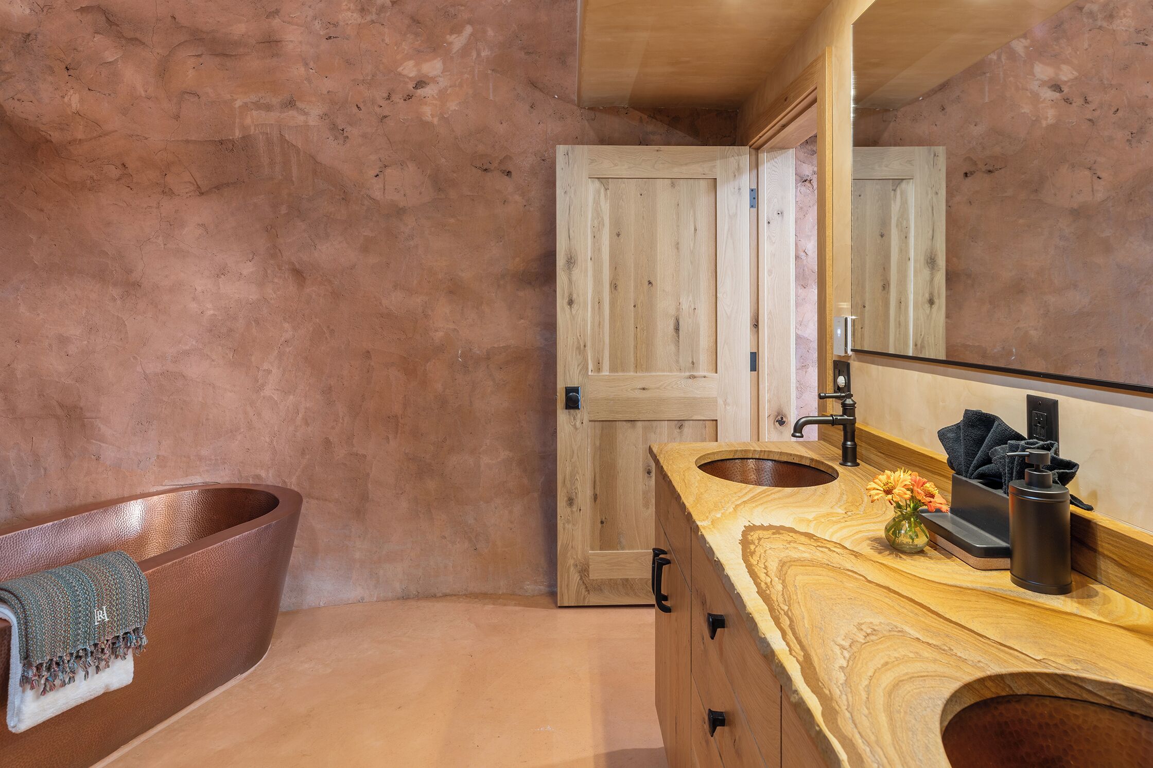 A bathroom with a wooden door, a sink with a marble countertop, and a towel rack.