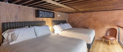 A room with two beds, wooden beams on the ceiling, and a wooden floor.