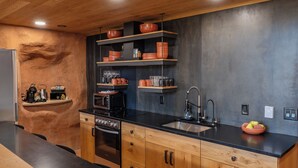 A modern kitchen with wooden cabinets, black countertops, and a built-in oven. There are shelves with kitchenware and a sink with a faucet. - Honey Rock Landing (Delta)