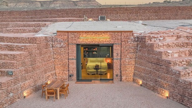 A hotel entrance with a brick facade, a glass door, and a seating area with a table and chairs. - Honey Rock Landing (Delta)