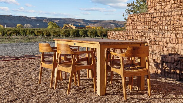 A wooden table and chairs set outdoors with a view of a vineyard and distant hills. - Honey Rock Landing (Delta)