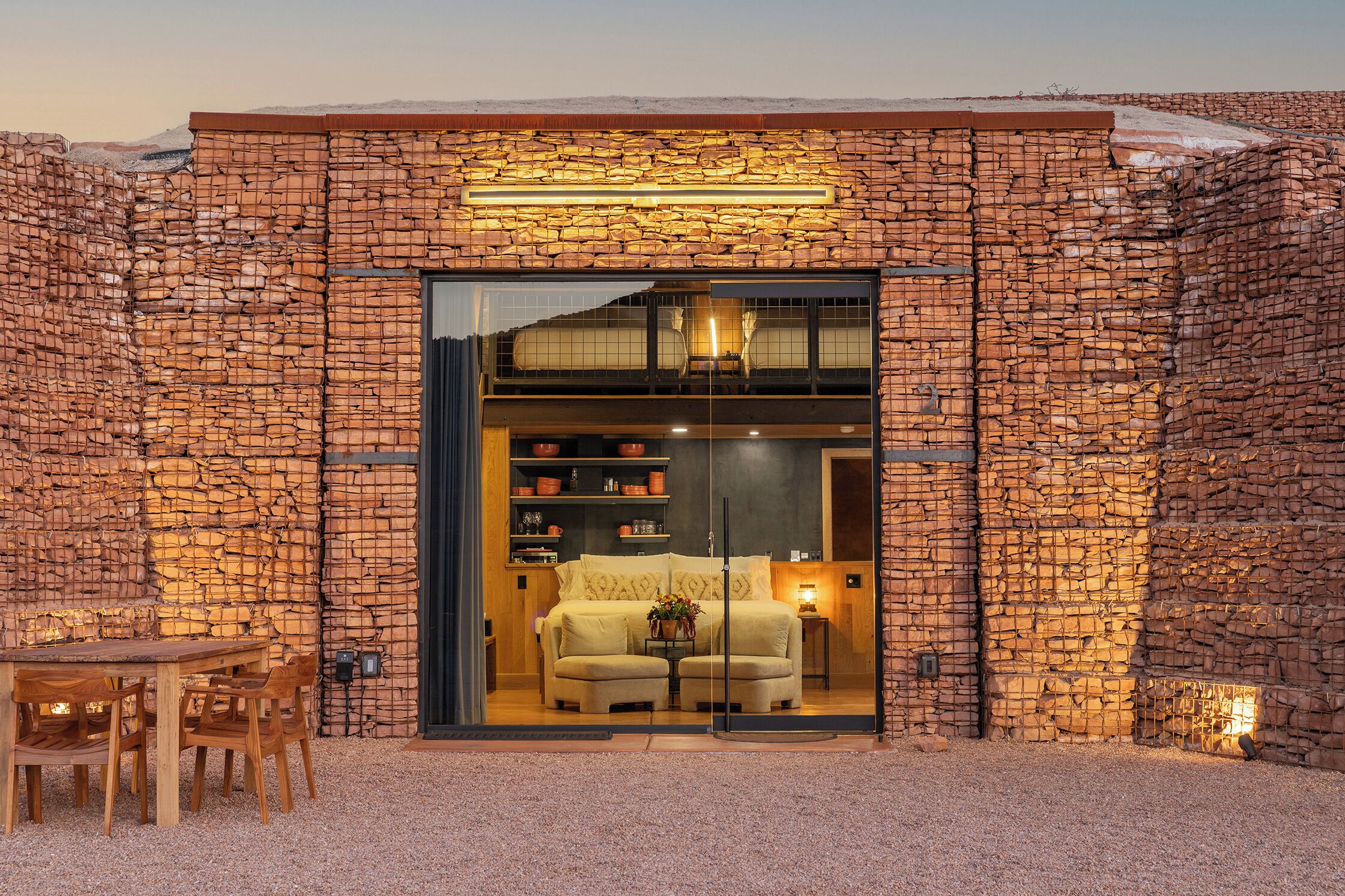 A modern building with a stone facade, a glass entrance, and a cozy interior with a sofa and dining area.