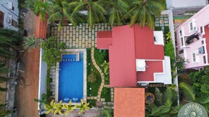 Vista aérea de una zona residencial con piscina, edificios de techo rojo y palmeras.