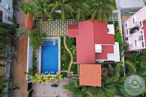 Vista aérea de uma área residencial com piscina, edifícios de telhado vermelho e palmeiras.