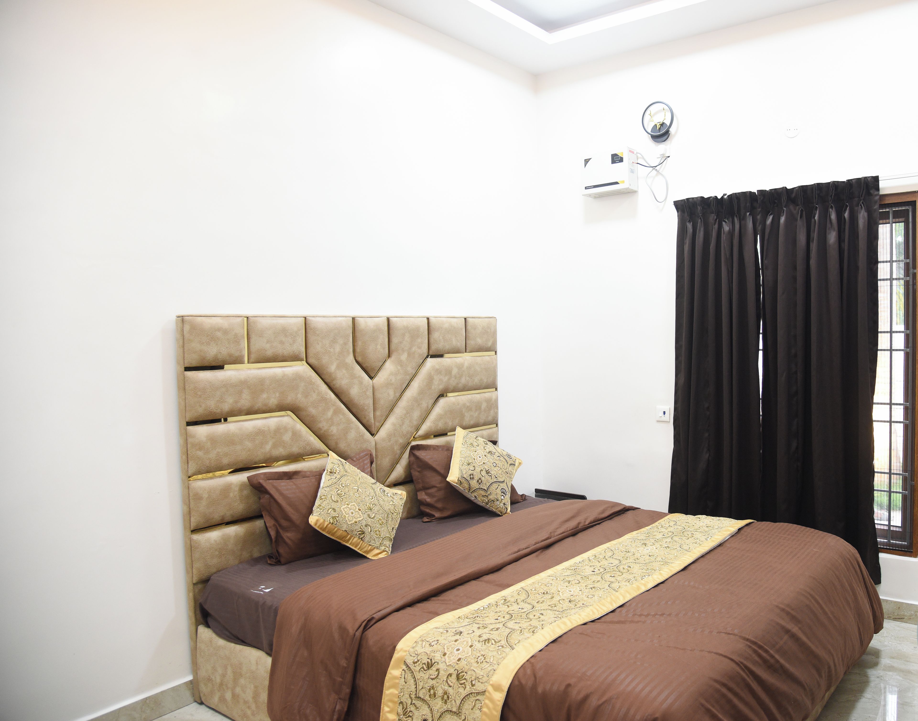 A bedroom with a tufted headboard, a brown bedspread, and a window with black curtains.