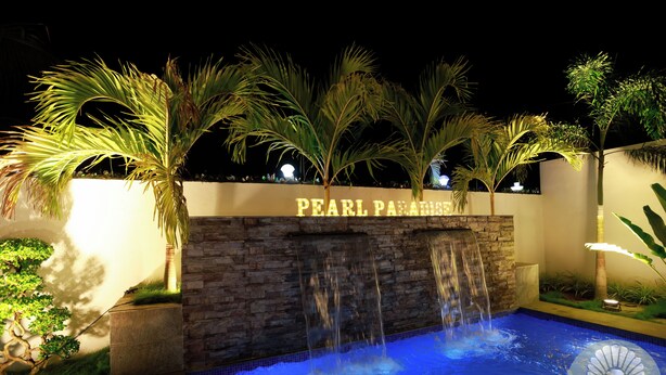 Vista nocturna de un área de piscina con cascada y palmeras, se ñalizada como 'PEARL PARADISE'.