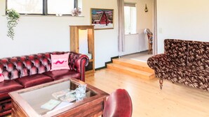 Un salon avec un canapé en cuir rouge, un fauteuil à motifs, une table basse en bois et un escalier menant à l’étage supérieur.