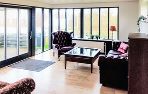 A spacious living room with a leather armchair, a glass-top coffee table, and a sofa. Large windows offer a view of the outdoors. - 1 bedroom nice home in Hurup Thy (Hurup Thy)