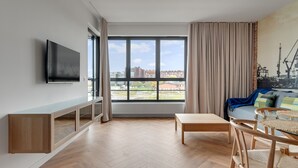Un salon moderne doté d’une grande fenêtre, d’un téléviseur à écran plat, d’un banc en bois et d’un canapé offrant une vue sur le paysage urbain.