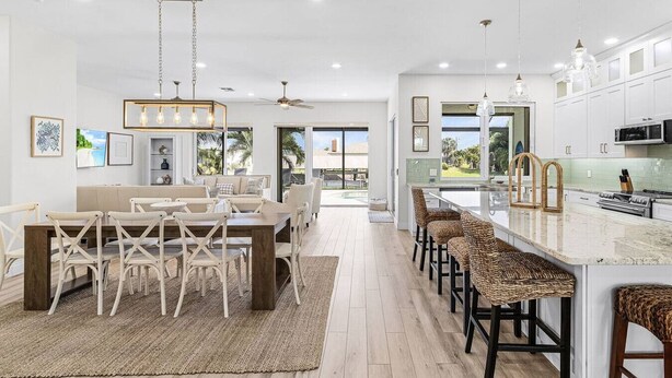 Una cocina moderna con armarios blancos, una isla central y una zona de comedor con sofá y sillas.
