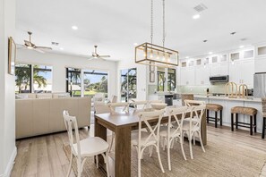 Uma cozinha moderna com armários brancos, uma área de jantar com mesa e cadeiras de madeira, e um ventilador de teto.