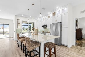 Cozinha moderna com uma ilha grande, banquetas, eletrodomésticos de aço inoxidável e vista para o exterior.