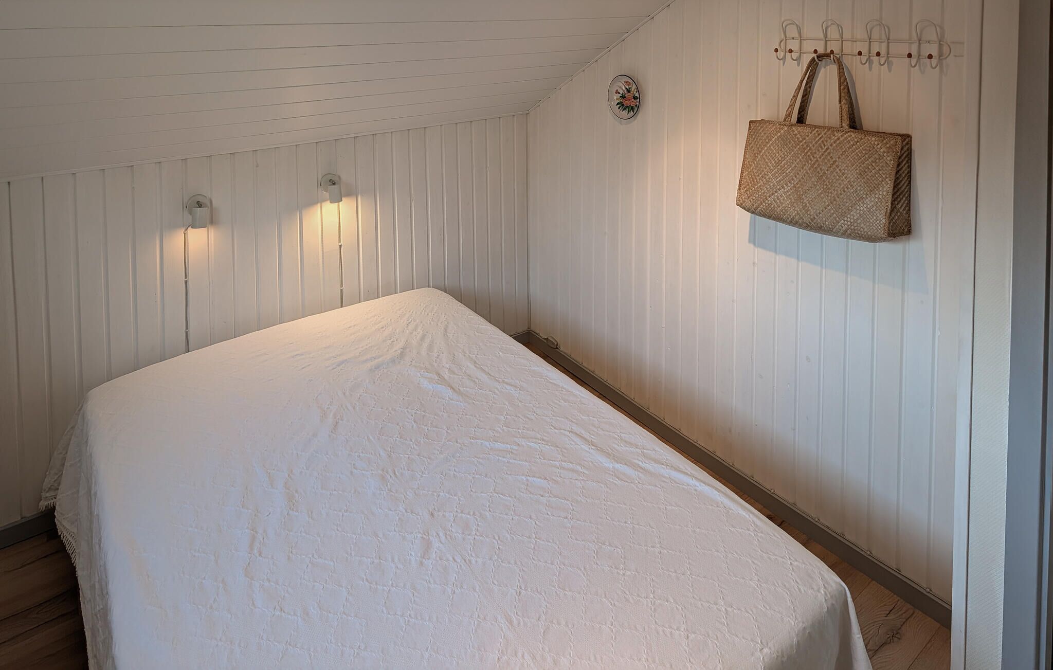 A bedroom with a bed, a wall-mounted clock, and a hanging bag.