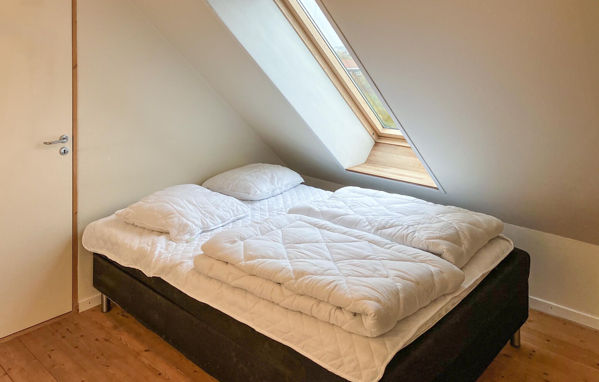 A bedroom with a sloped ceiling and a skylight, featuring a bed with white bedding.