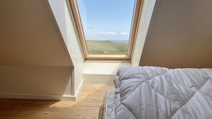Ein Schlafzimmer mit Dachfenster, Holzboden und einem Bett mit weißer Bettwäsche.
