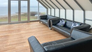 Ein modernes Wohnzimmer mit Holzboden, zwei schwarzen Ledersofas und einem großen Glasfenster mit Blick auf das Meer.