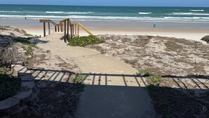 A beach pathway leading to the ocean with a wooden structure and a person walking.