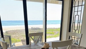 A dining area with a table and chairs, a view of the beach, and a door with a metal gate.