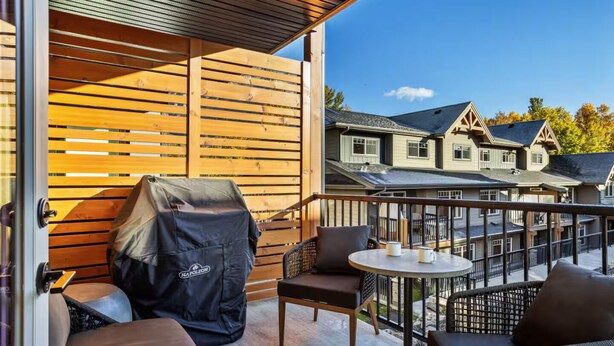 A balcony with outdoor furniture, a covered grill, and a view of residential buildings.