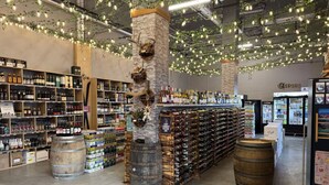 A spacious store with shelves stocked with various bottles and boxes, a central pillar with a decorative tree, and a counter with more bottles.