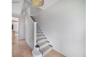 Eine Treppe mit weißer Geländer und beigen Teppichstufen, die zu einer Zwischenebene führen.
