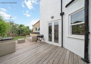 Eine Außenterrasse mit Korbmöbeln, einem Grill und einer Glasschiebetür, die auf eine Terrasse führt.