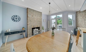 A dining room with a large wooden table, a brick fireplace, and a clock on the wall.
